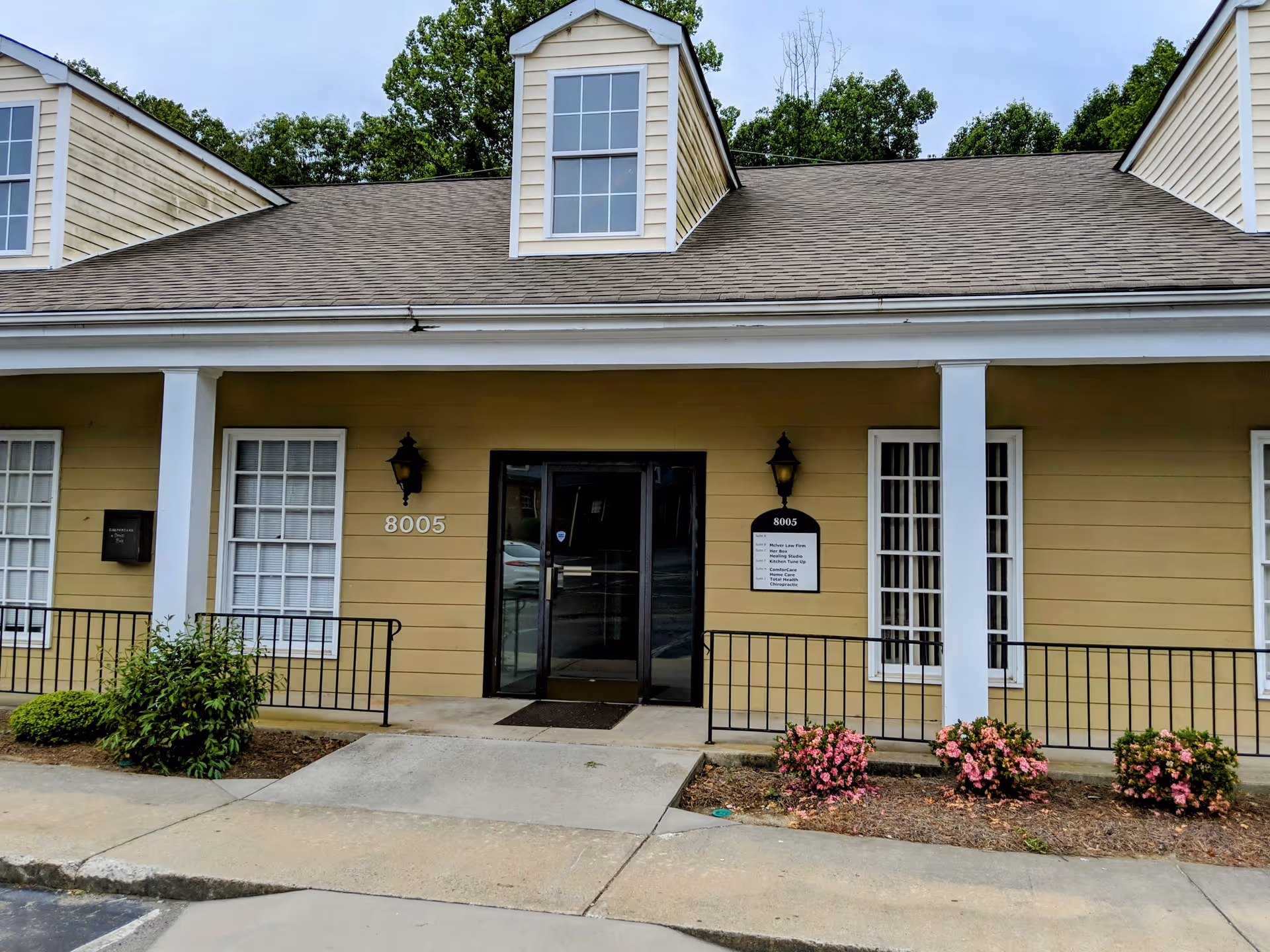 Front entrance of a yellow building with white columns and landscaped shrubs.
