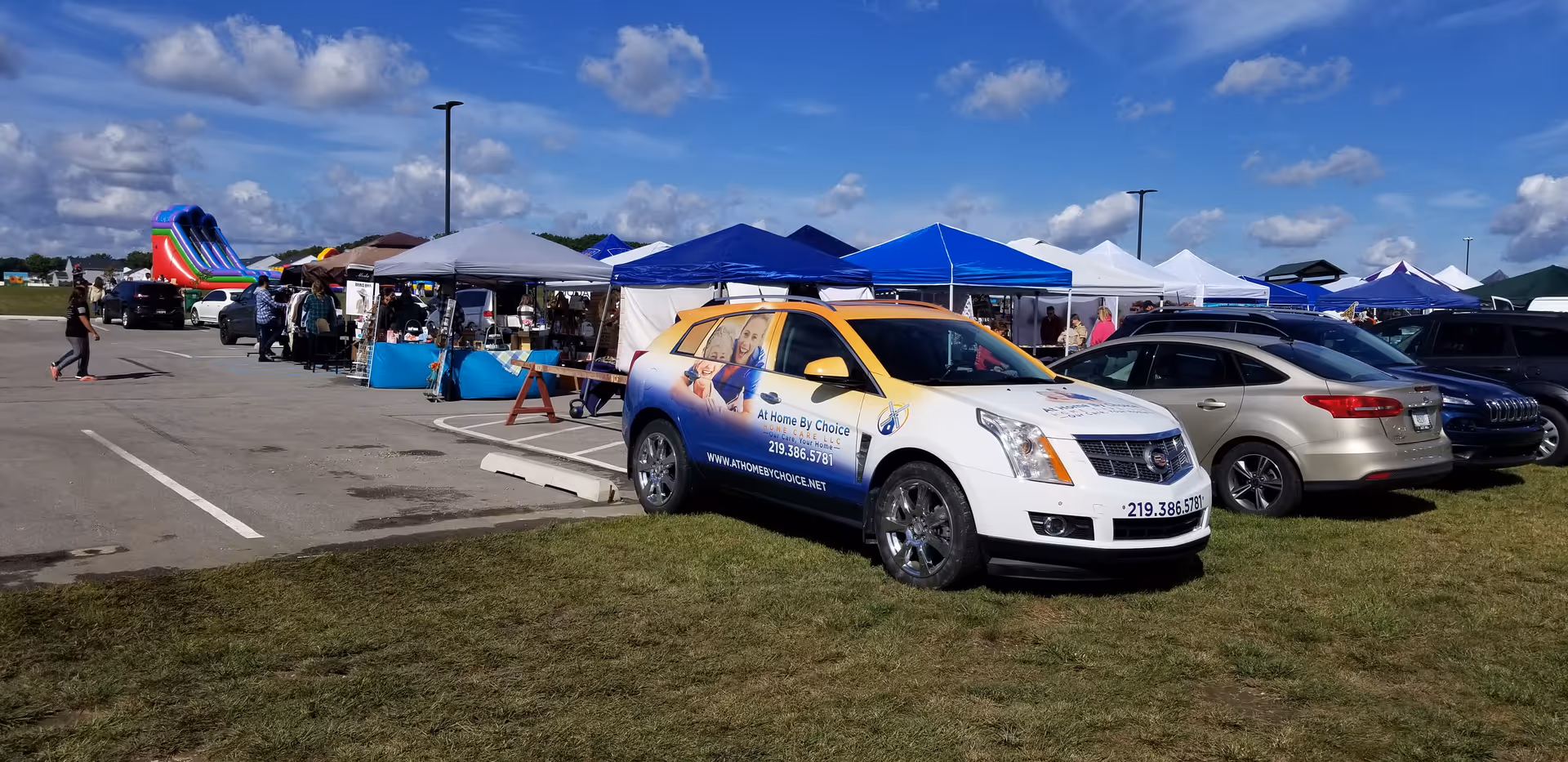 Outdoor vendor fair in a parking lot with tents and an At Home By Choice van.