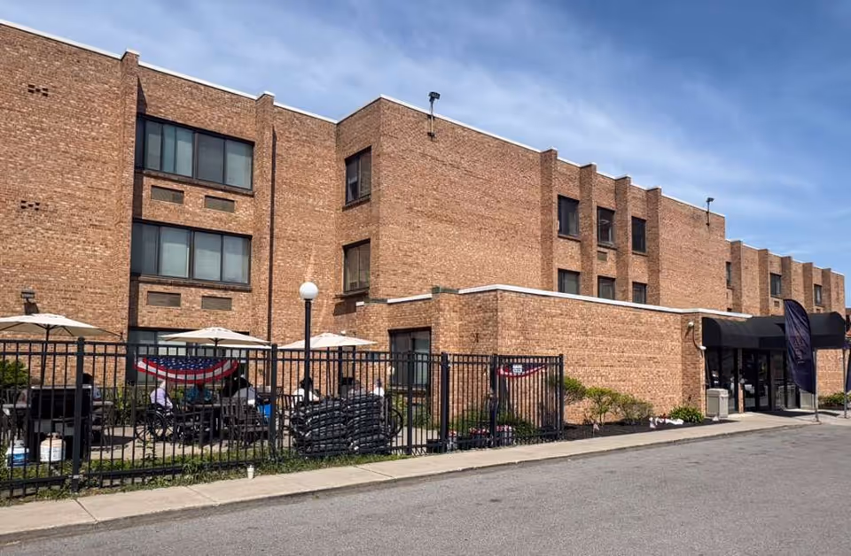 The brick senior living center exterior shows a fenced outdoor patio with residents seated.