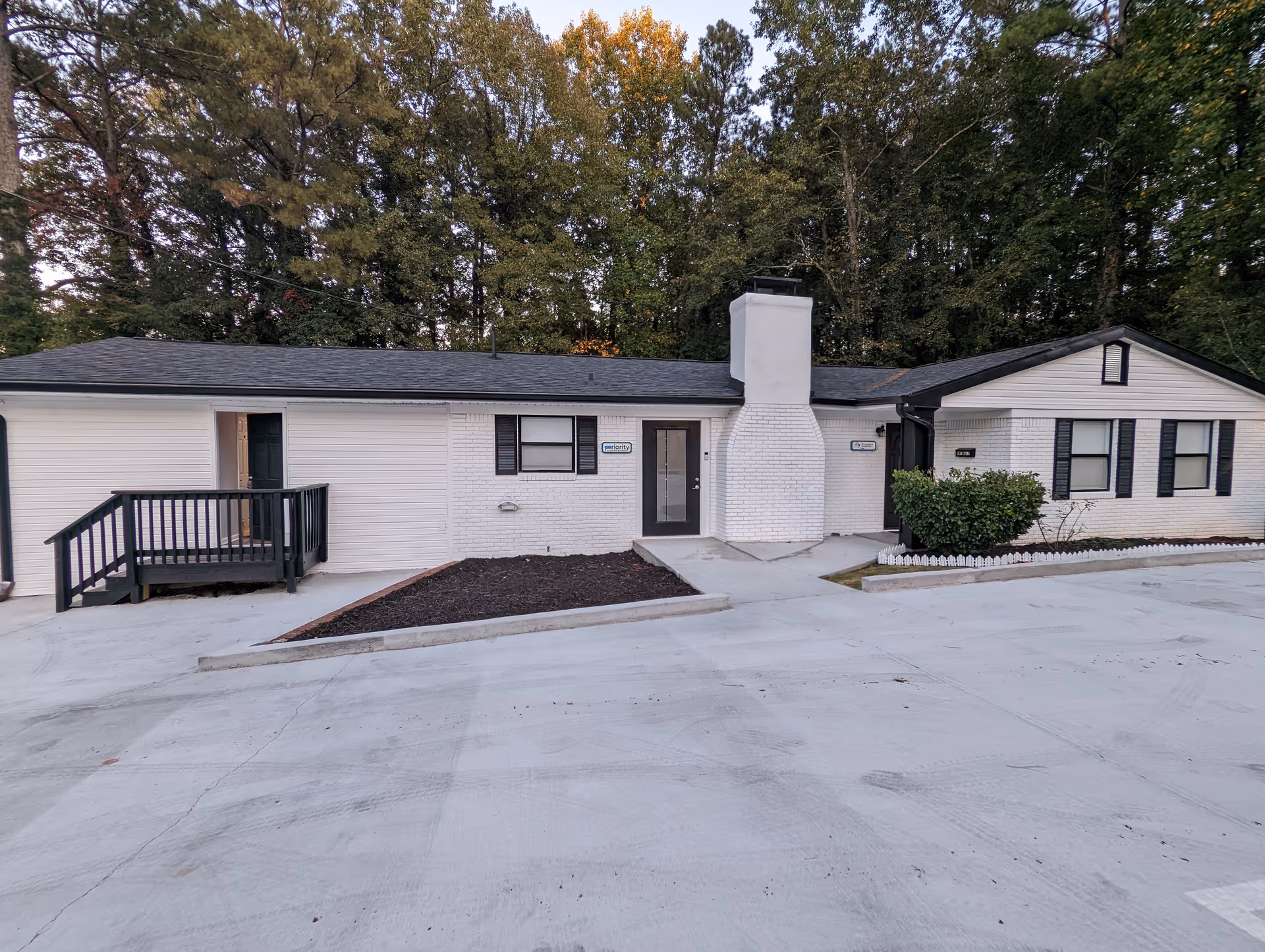 White single-story senior living facility exterior with a paved parking lot and trees behind.