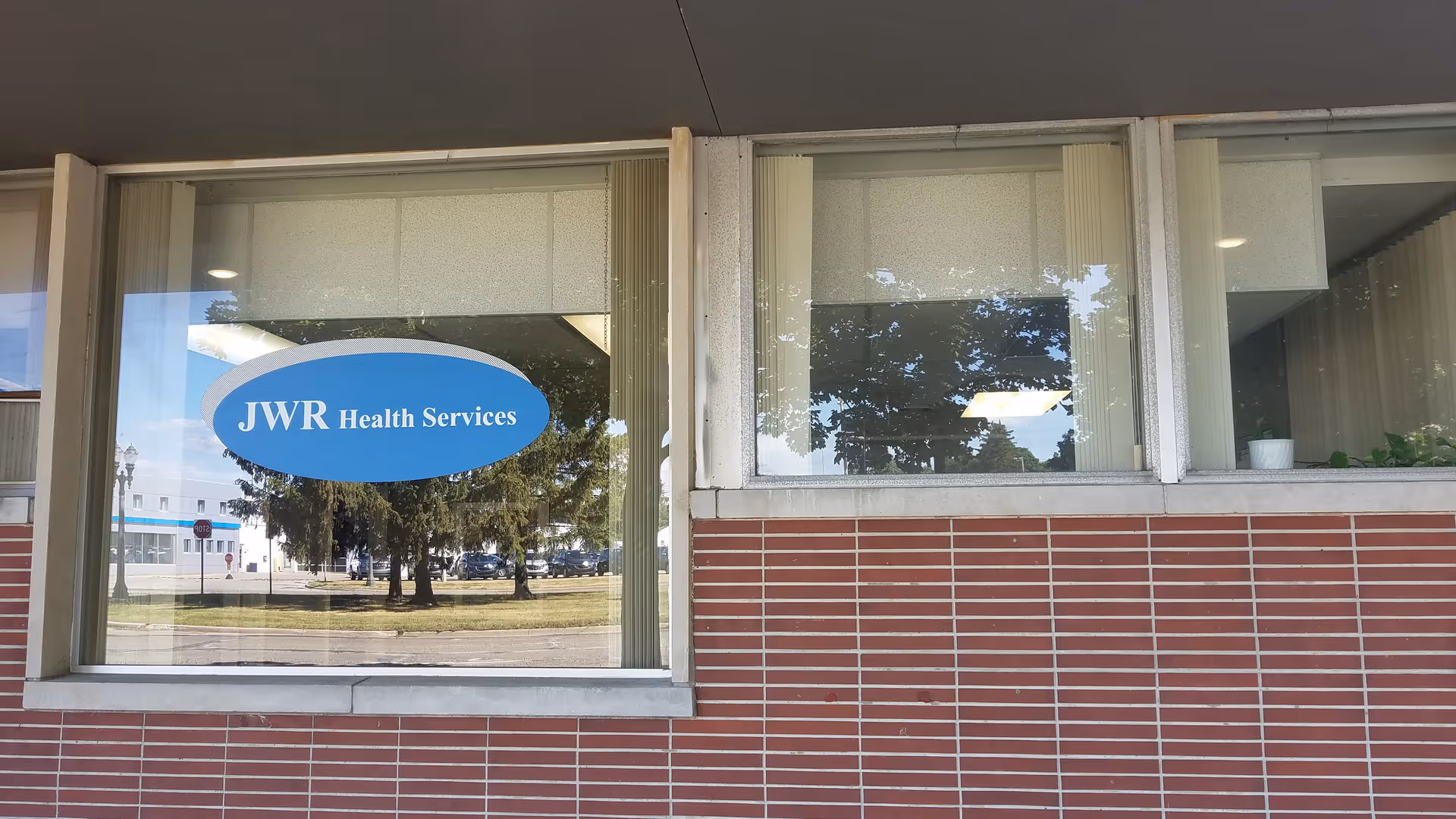 Exterior of JWR Health Services building with a blue oval sign on the front window.