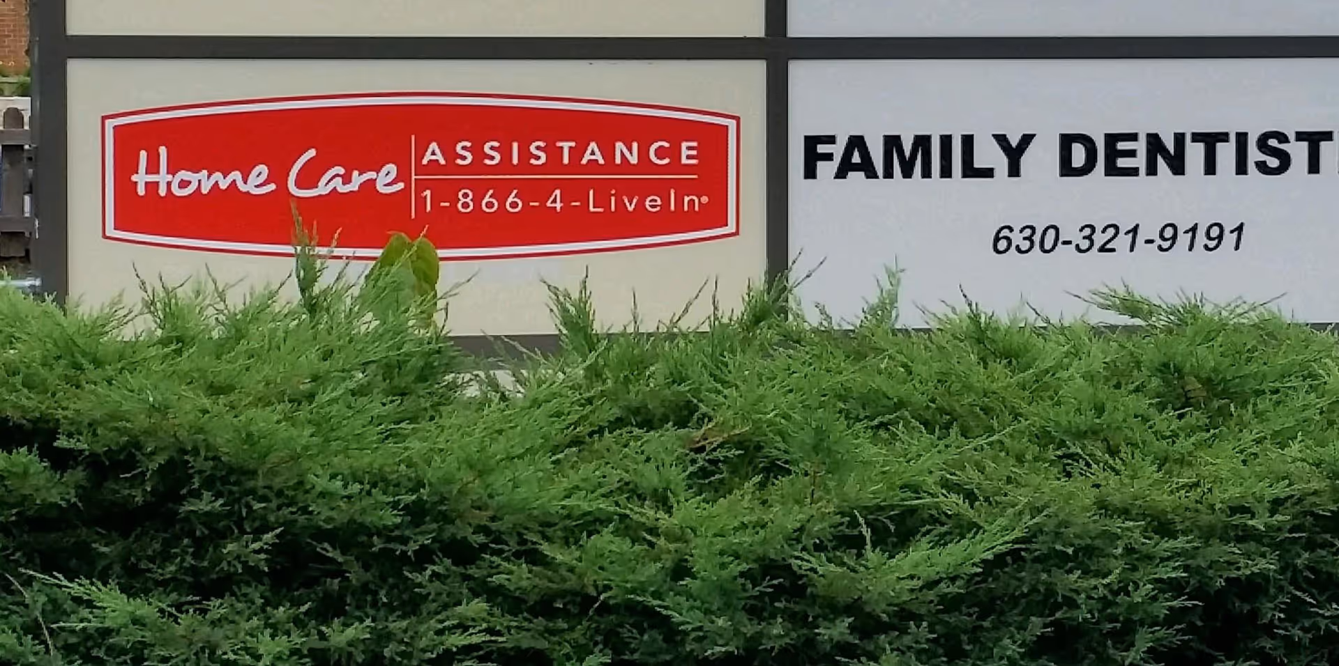 Exterior building front signs for Home Care Assistance and Family Dentistry with shrubs.