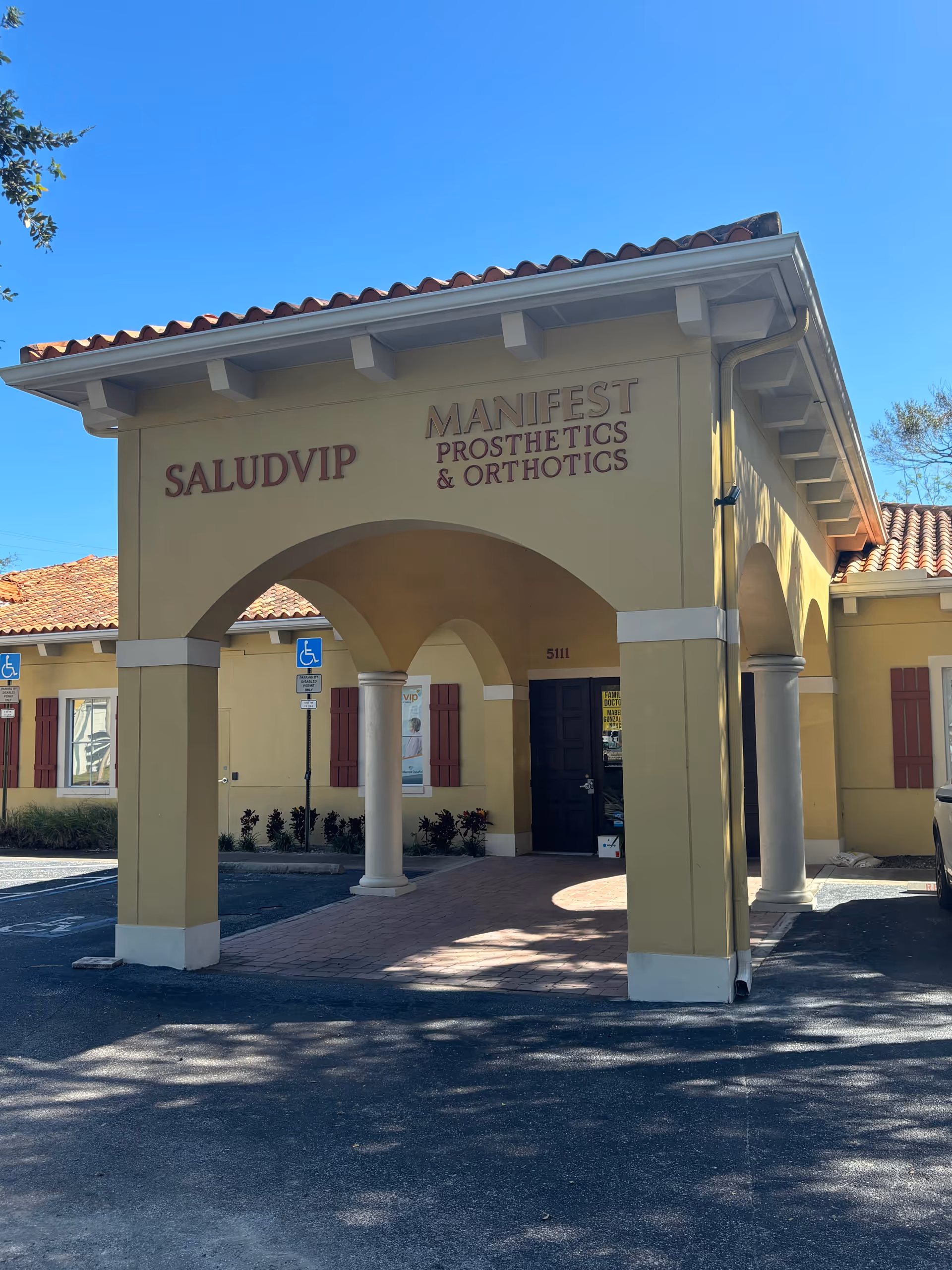 Front entrance of a yellow building with arches and Manifest Prosthetics & Orthotics signage.