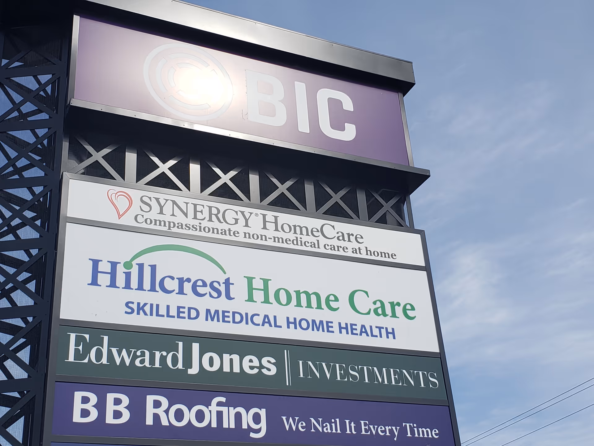 Tall exterior sign structure displays Hillcrest Home Care and other business signs against blue sky.