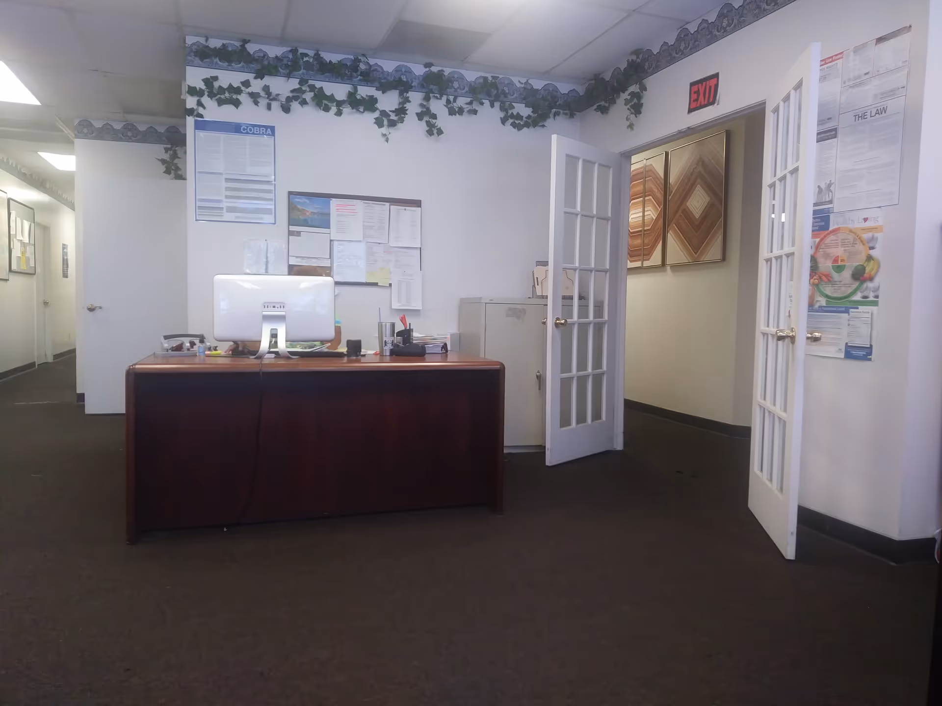 Reception desk with computer and paperwork inside facility lobby, French doors opening to hallway.
