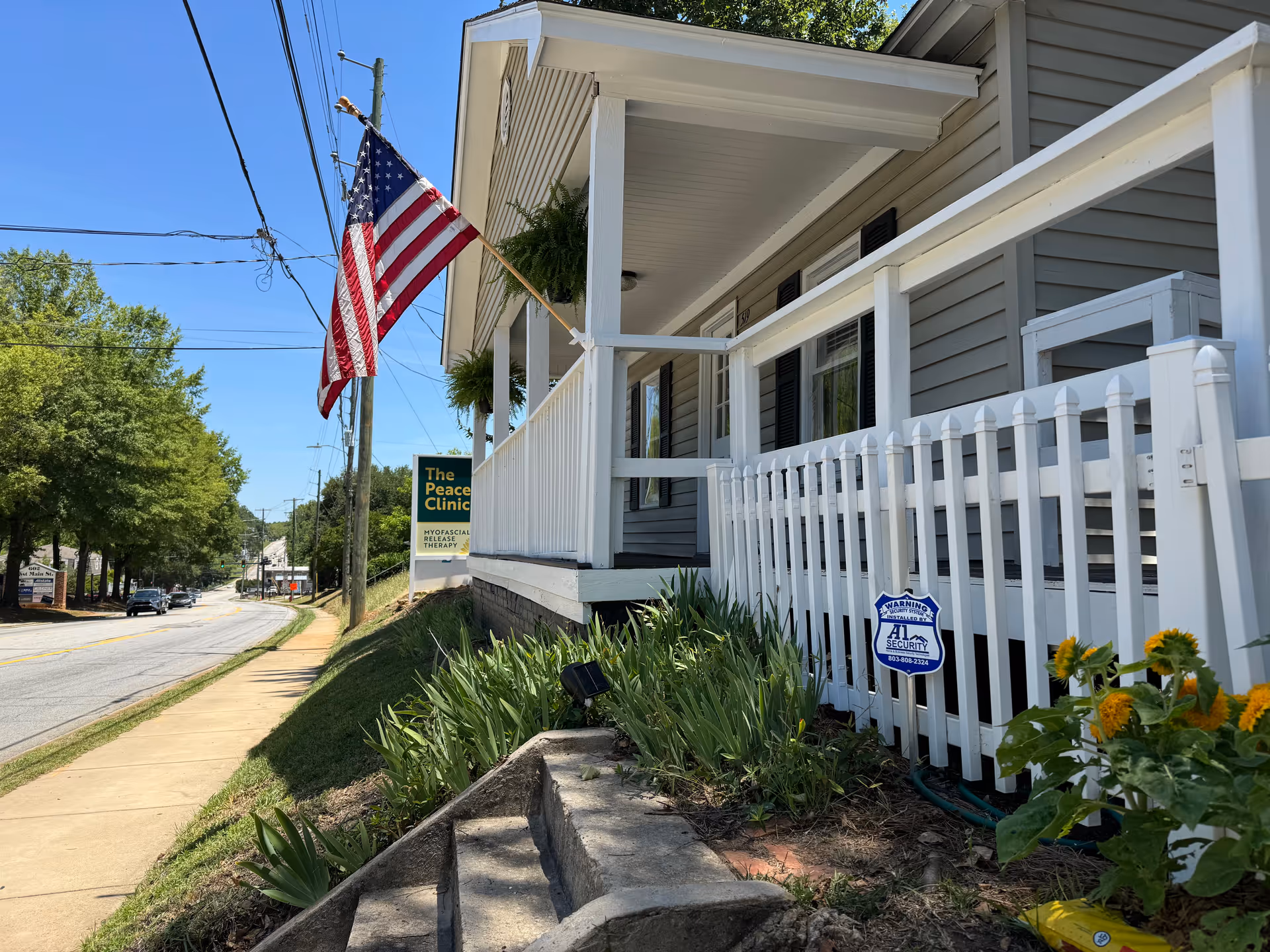 Exterior view of a gray building with white porch, flag, and landscaped front yard.