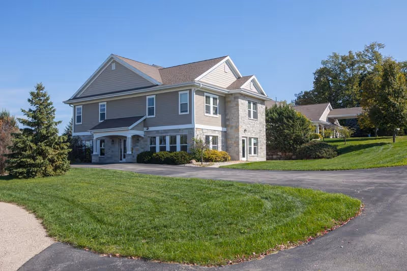 Two-story assisted living building with stone façade and curved driveway on green grounds.