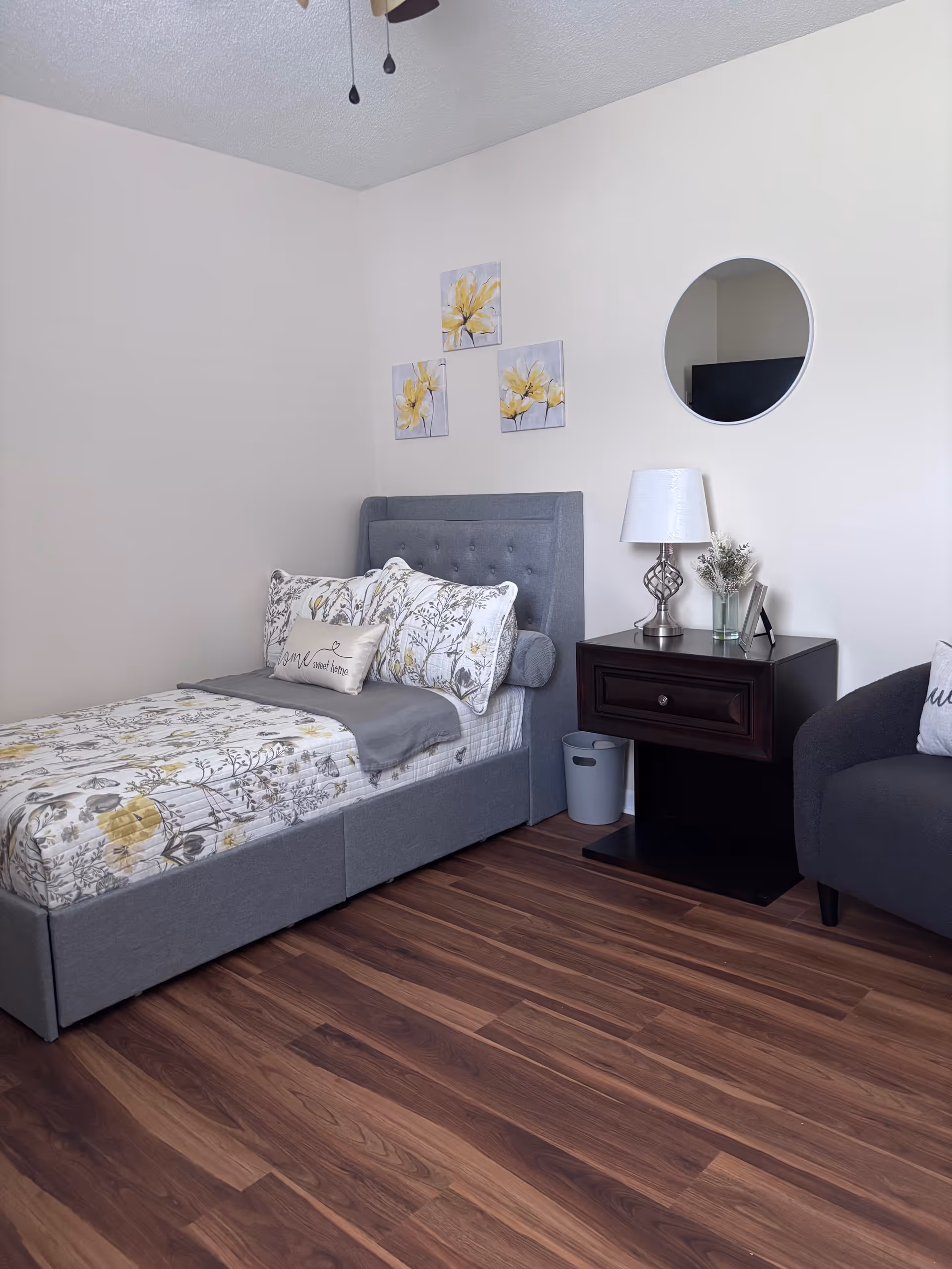 Cozy gray bedroom featuring bed, nightstand, decorative pillows, and round mirror.