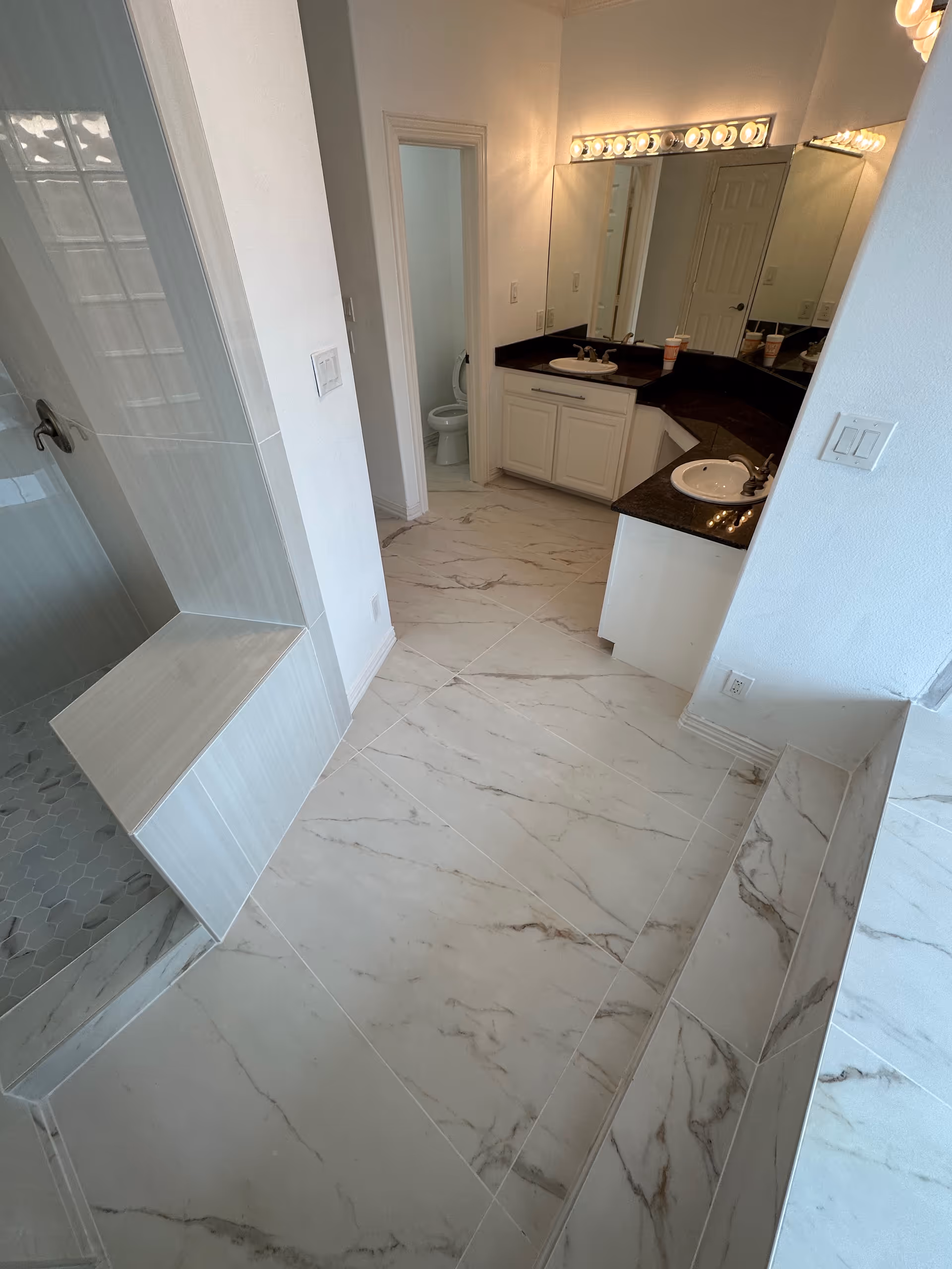 Modern bathroom featuring double-sink vanity, marble floors, shower, and adjacent toilet.