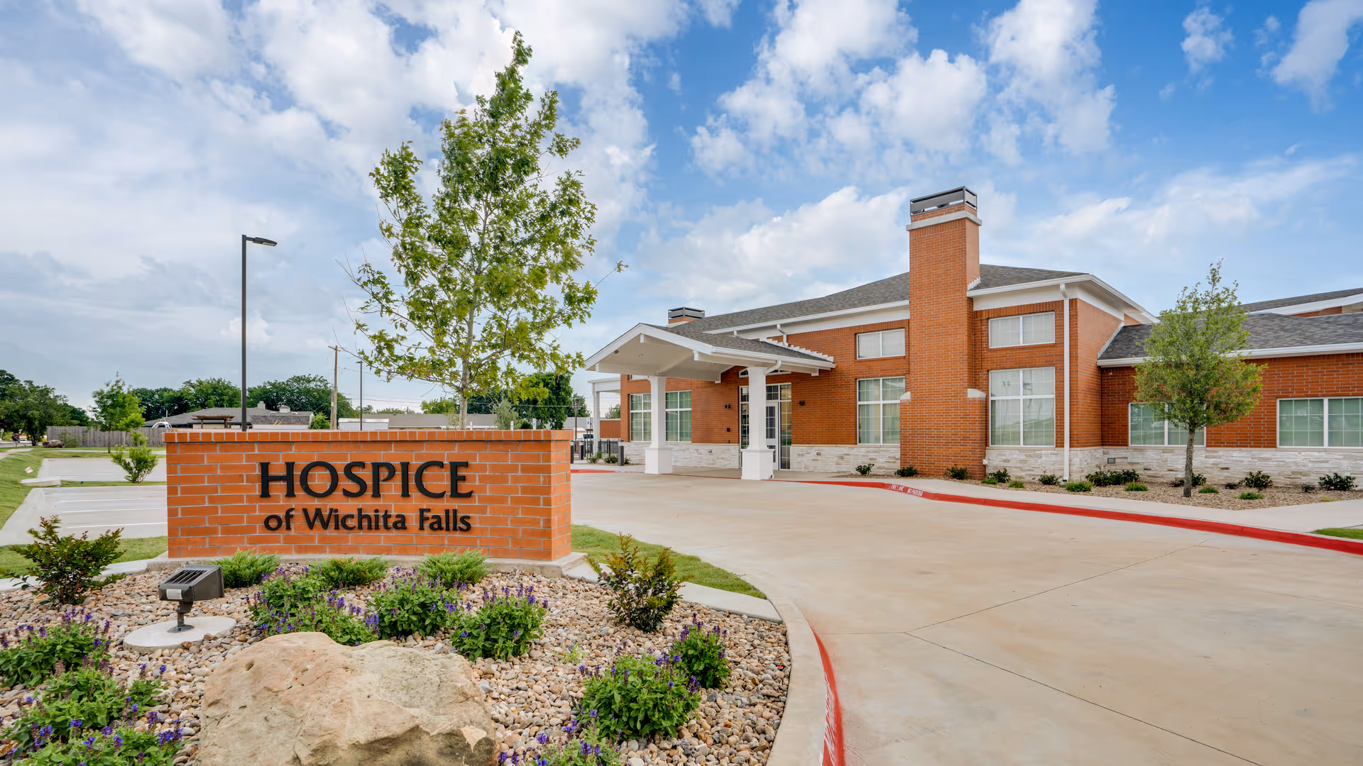 Brick hospice facility with sign and landscaped driveway entrance.