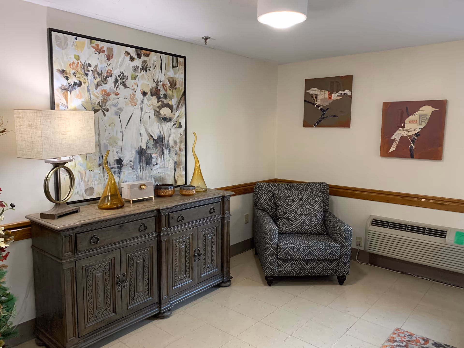 Cozy living area with a patterned chair, sideboard, lamp, and abstract art.