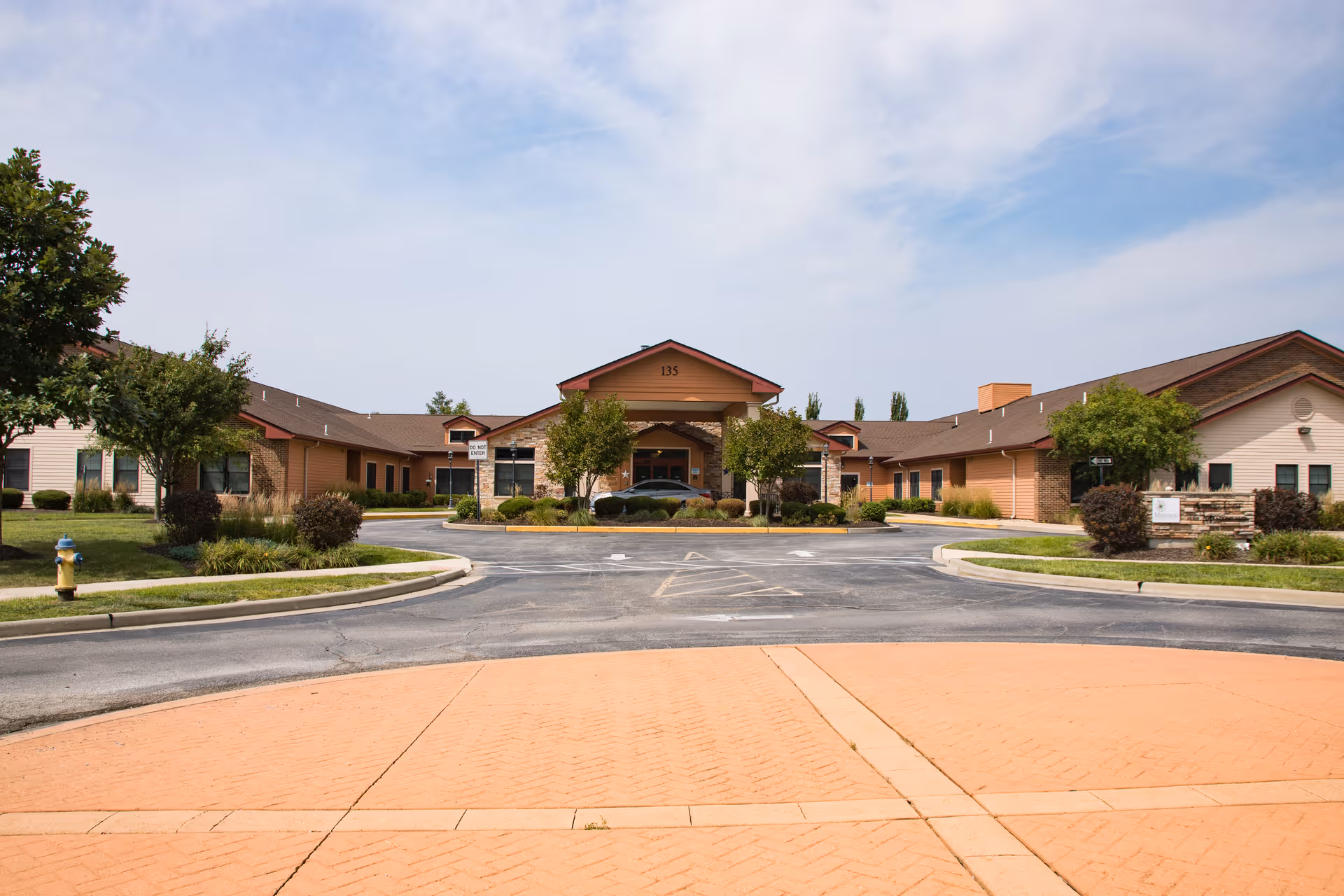 Front entrance of a single-story senior living facility with a covered portico, circular driveway, and landscaped lawns.