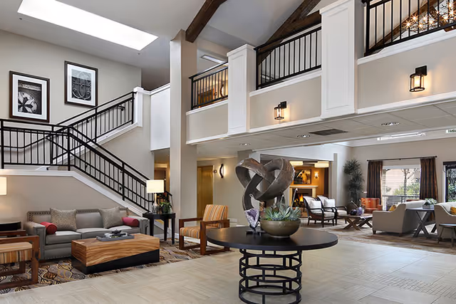 Well-lit spacious senior living lobby with a staircase, modern seating, and sculpture.