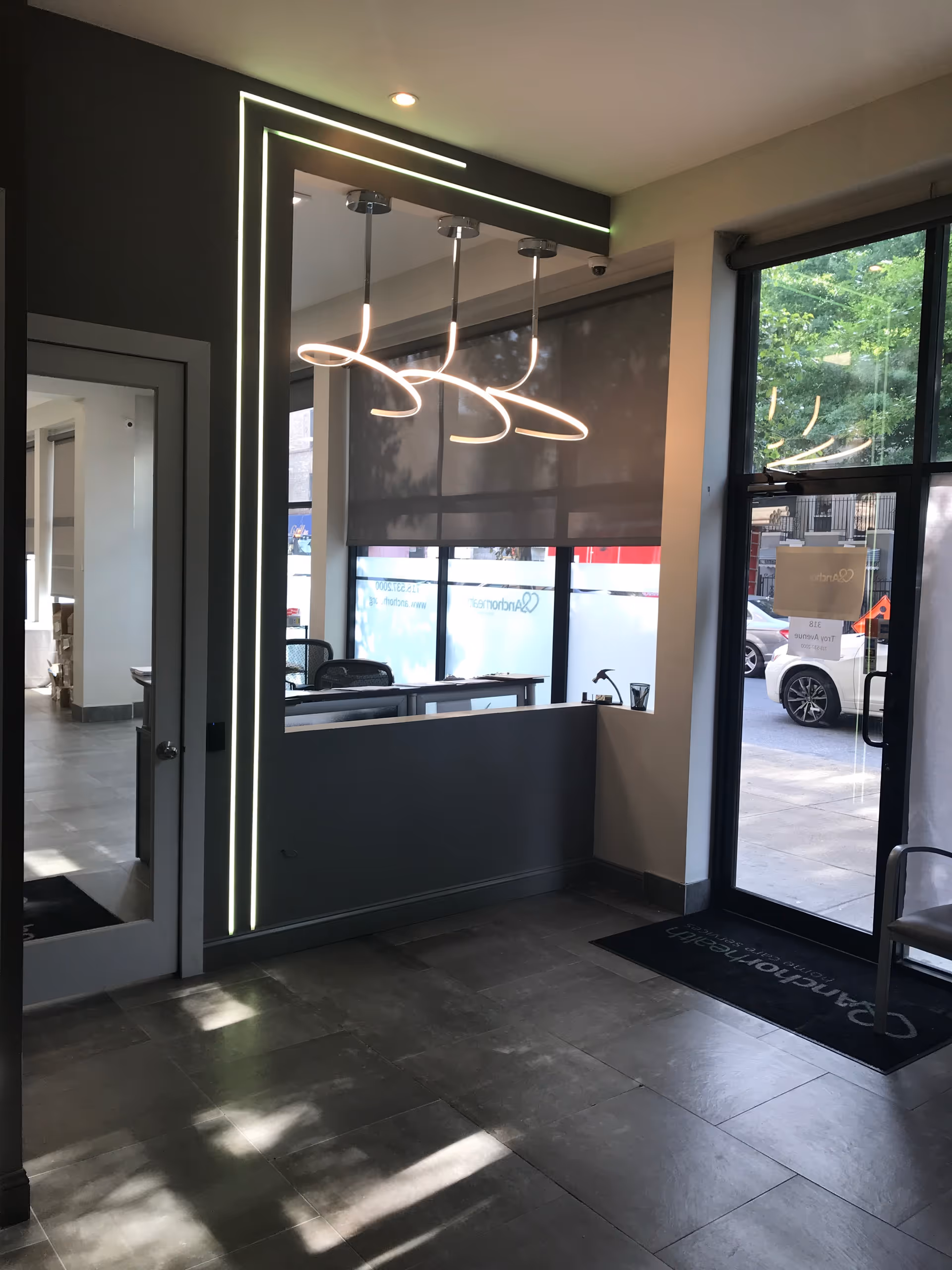 Modern facility lobby with illuminated mirror frame, hanging lights, and a glass entry door.