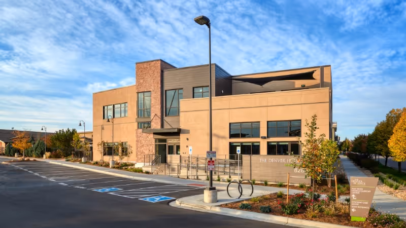 Front view of The Denver Hospice building with parking lot and blue sky.