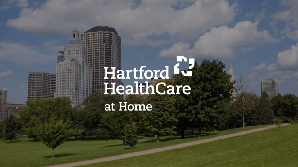 Hartford HealthCare at Home logo over a city park with trees and a skyline