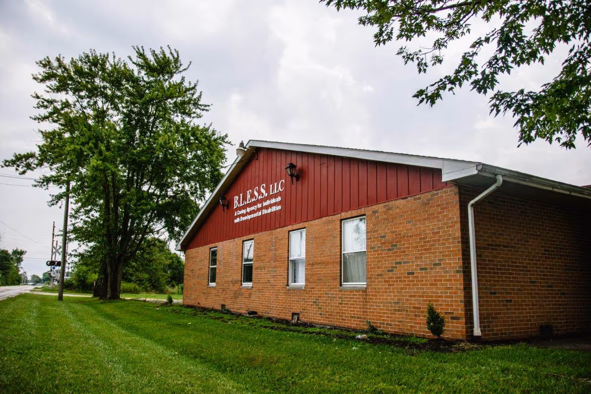 Brick building front with red gabled sign reading BLESS LLC and green lawn.