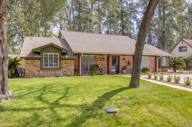 Front exterior of a single-story brick senior living facility with a manicured lawn.