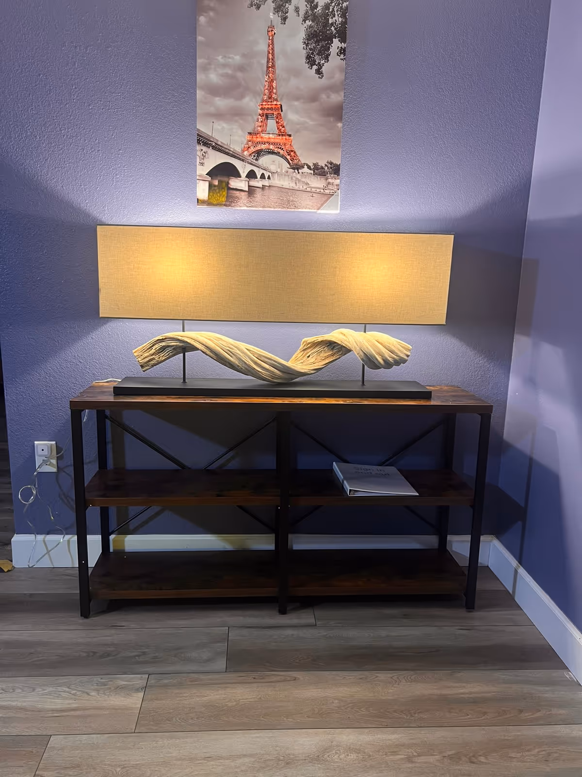 Purple-walled interior with console table, sculpture, lamp, and Eiffel Tower wall art.