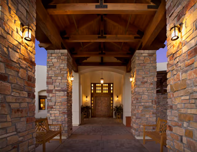 Stone pillars frame a covered entrance with wooden beams and benches.