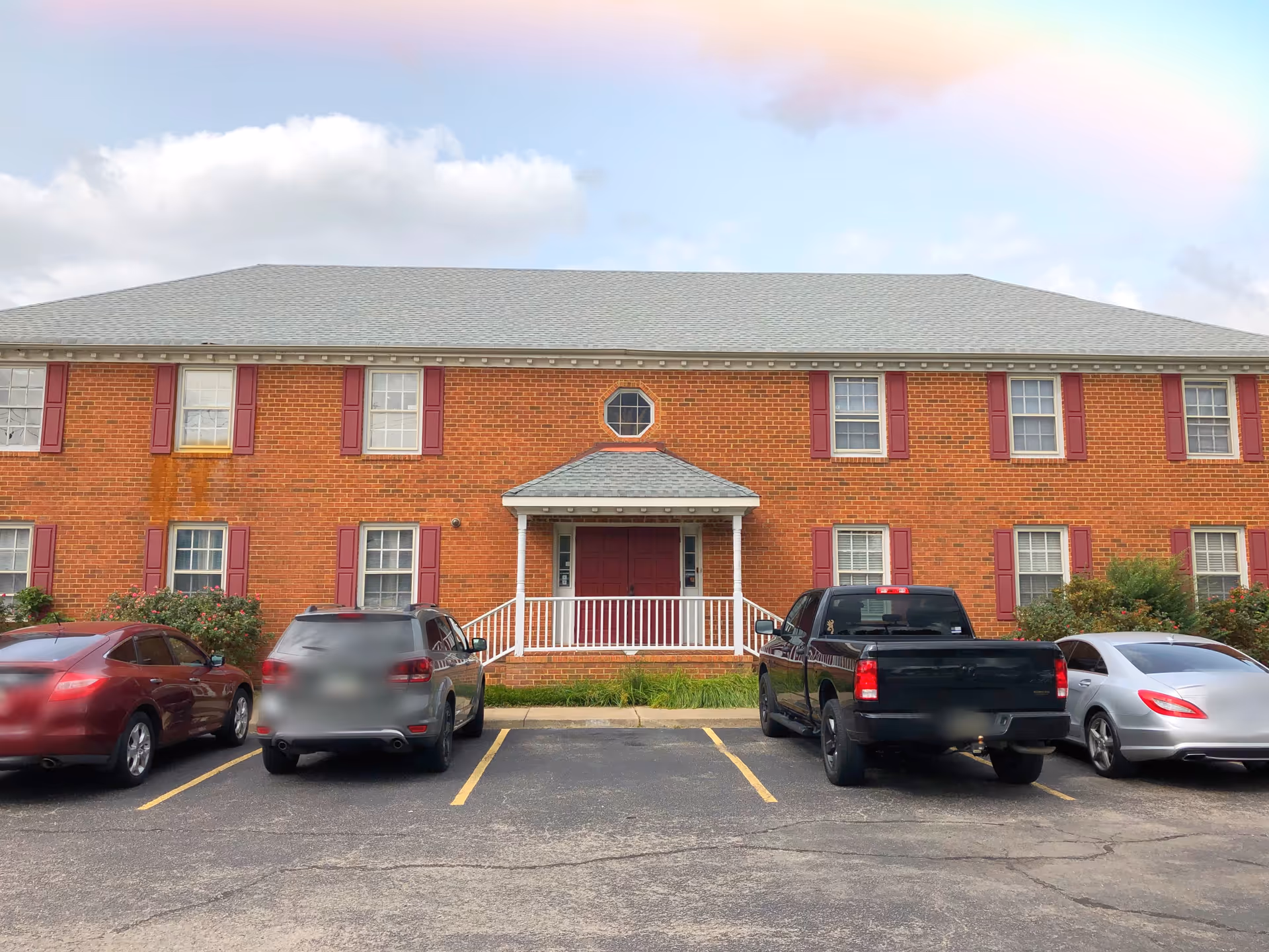 Brick senior living facility exterior with a small porch and parked cars.