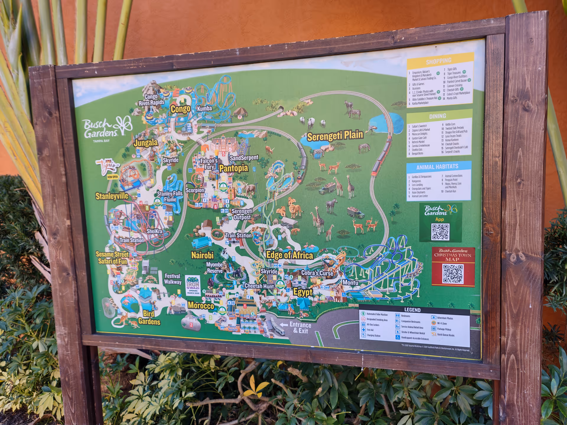A large colorful map sign mounted on wood frame outdoors, surrounded by greenery.