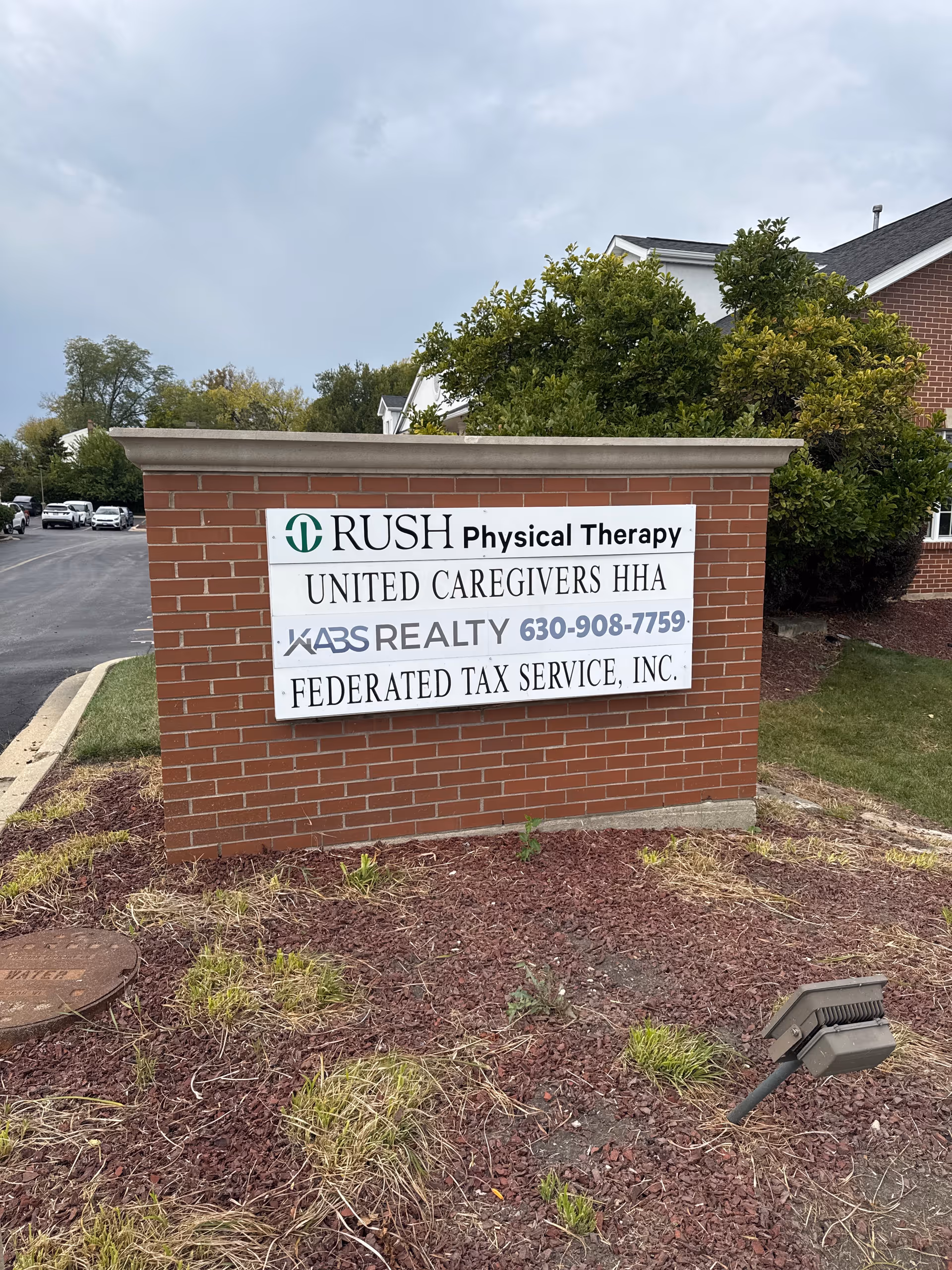 Brick sign displays Rush Physical Therapy and United Caregivers HHA outside a building.
