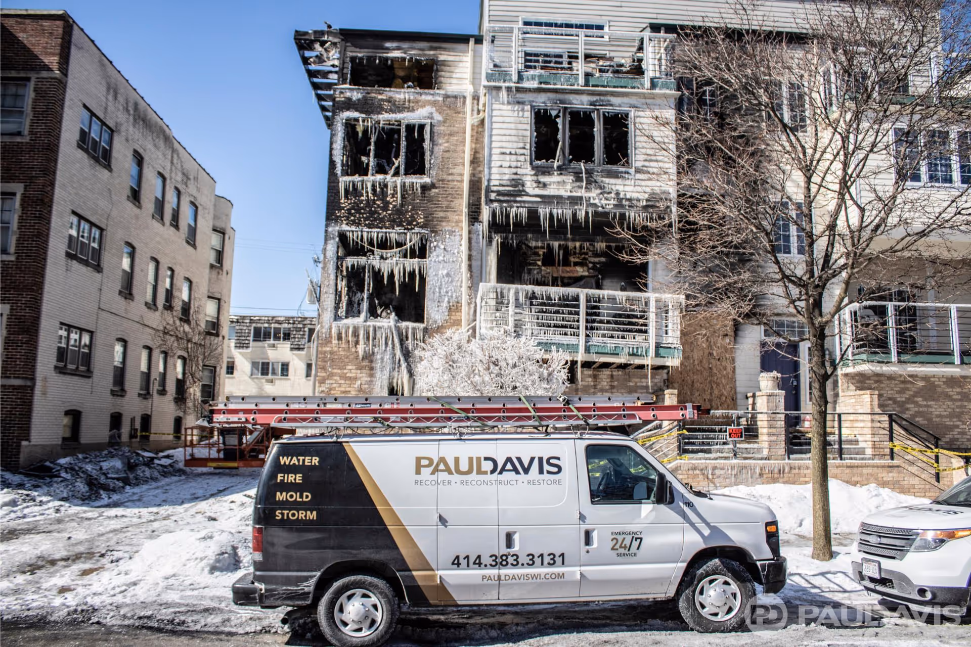Charred exterior of a multi-story building with icicles, snow, and Paul Davis restoration van in front