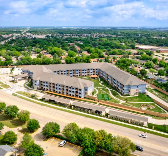 Aerial view of a large senior living campus with beige buildings and green lawns.