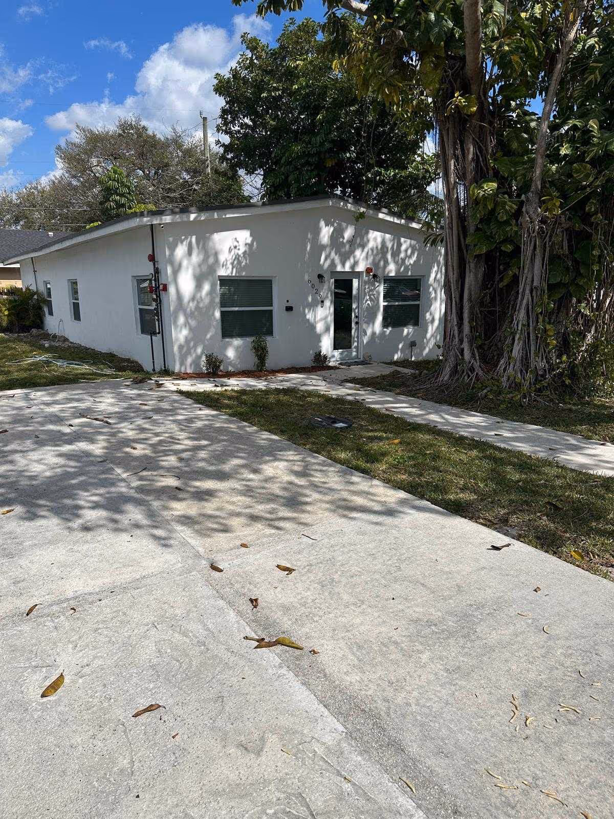 White single-story building exterior with windows, a door, and surrounding trees.