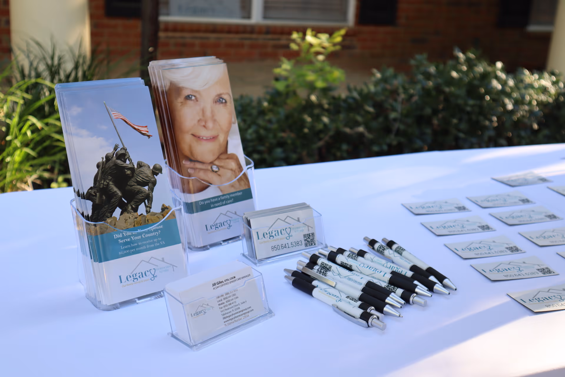 Legacy Homecare Group promotional table with brochures, pens, and name cards outside a brick building.