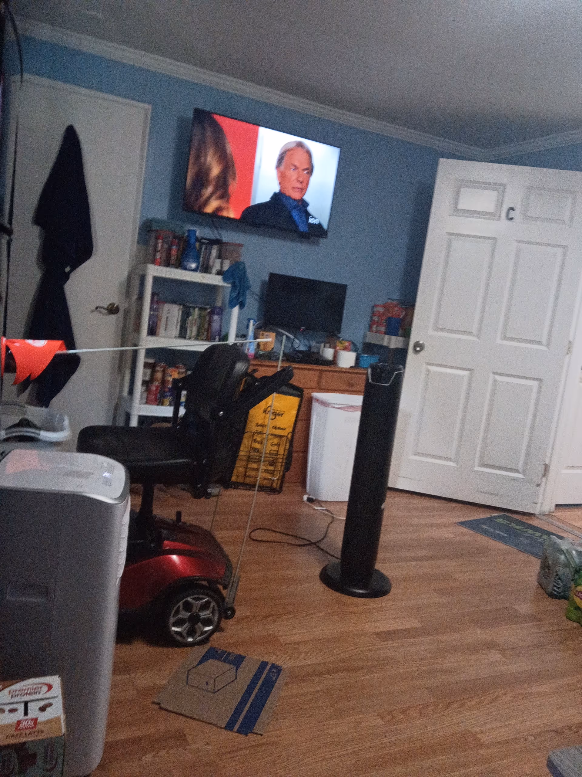 Cluttered senior living room with TV, chair, shelves, and a mobility scooter.