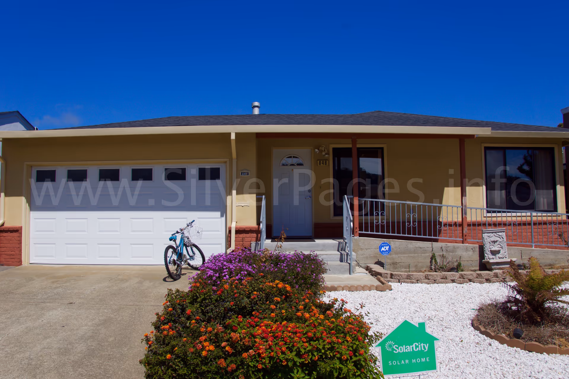 Bel Amor IV senior facility exterior: single-story beige building with garage, porch, and flowers.
