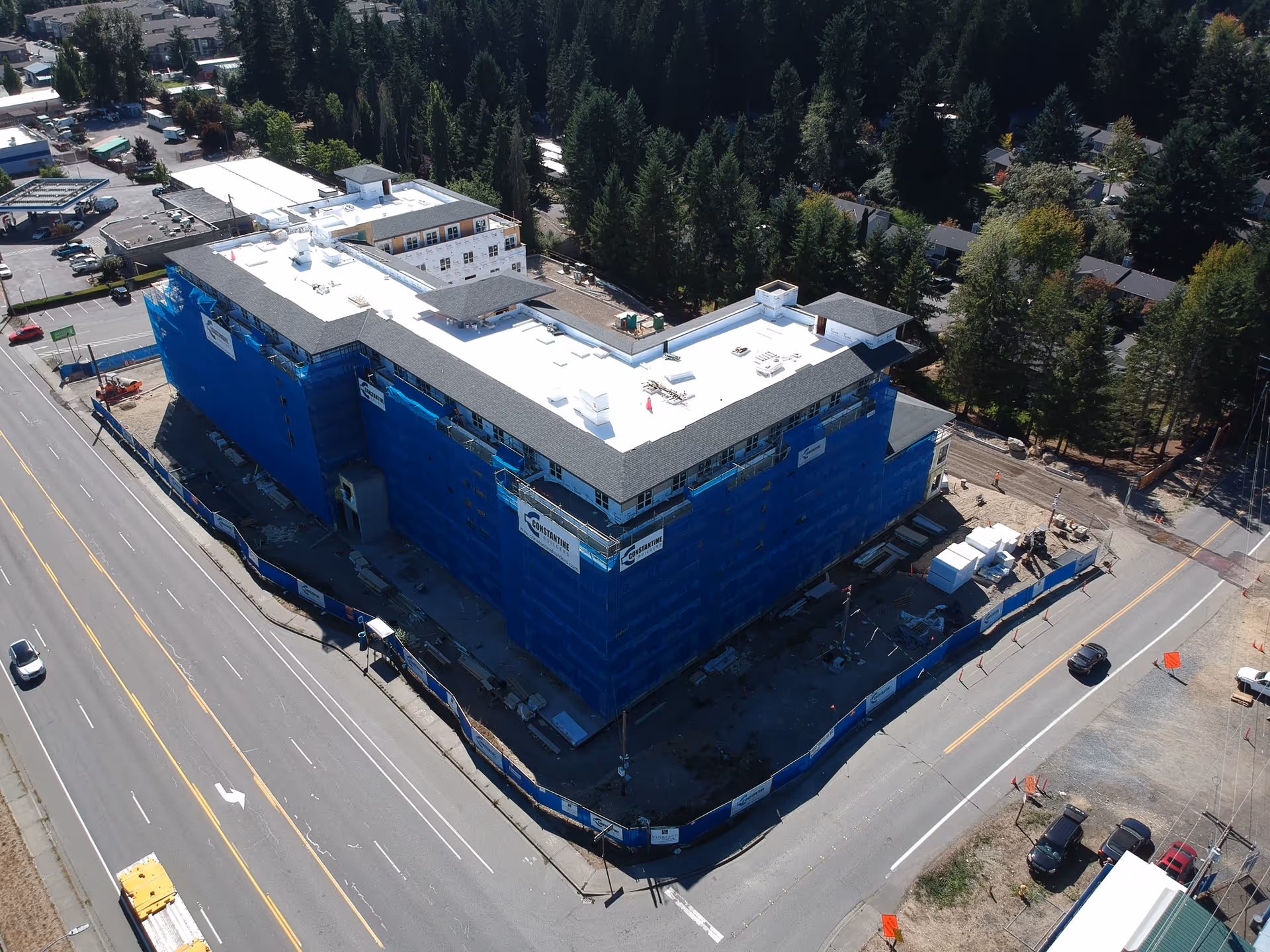 A large, multi-story building under construction wrapped in blue netting beside a road.