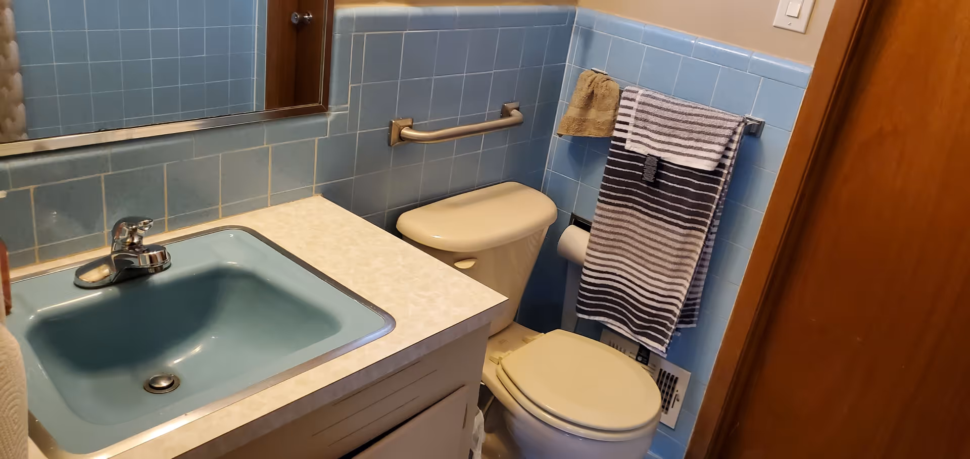 Blue-tiled bathroom with sink, toilet, and towels in a compact senior living unit.