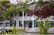 Front exterior of Jesmond Nursing Home with porch, white siding, and green umbrellas.
