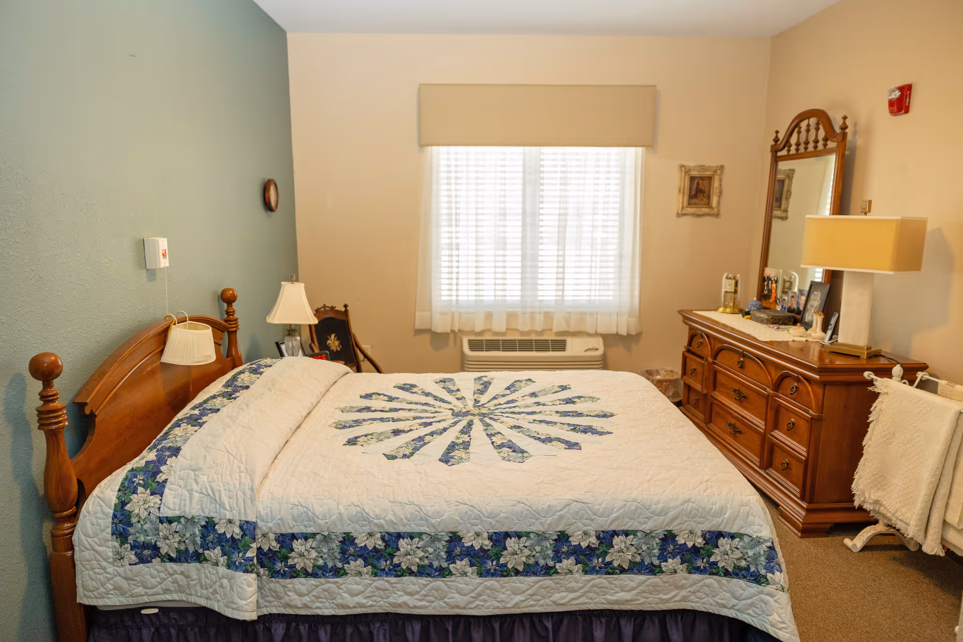 Cozy bedroom with a wooden bed, quilt, dresser with mirror, and window blinds.