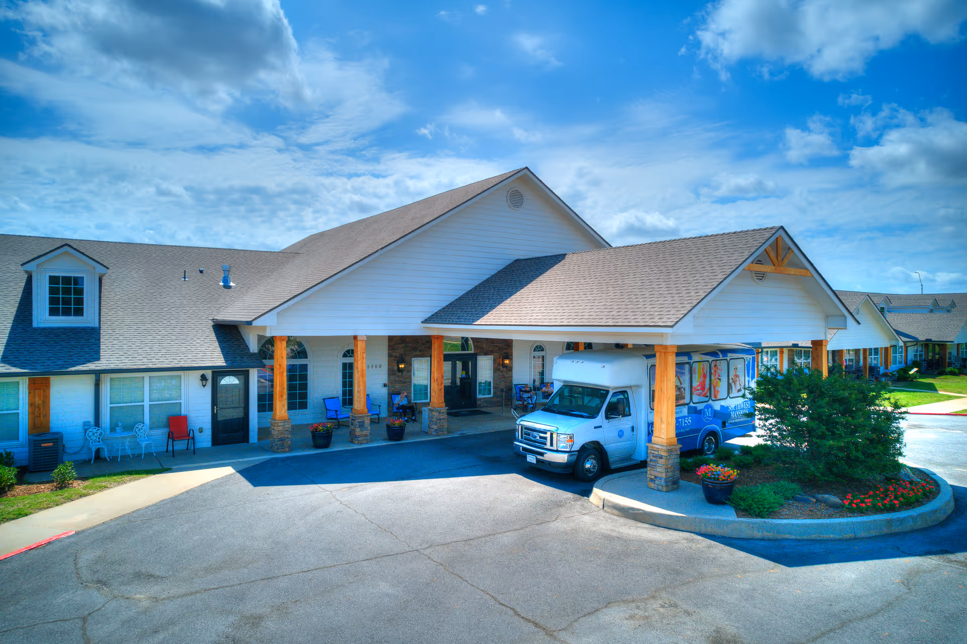 White, single-story senior living facility with a covered front entrance and a parked shuttle bus.