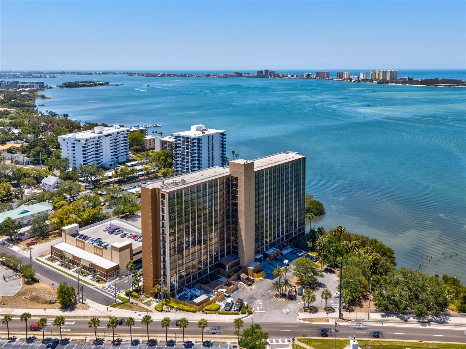 Aerial view of a tall waterfront senior living building and surrounding neighborhood overlooking a turquoise bay.