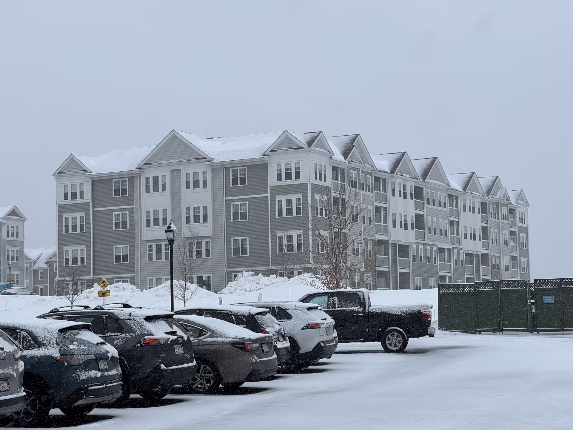 Snow-covered Chauncy Lake senior living building with parked cars in a snowy lot.