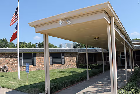 Single-story brick nursing facility with a covered entrance and flagpoles.