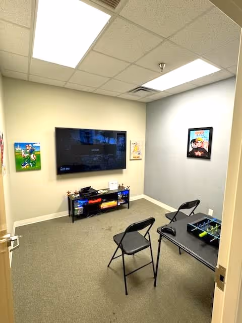 A small resident lounge with a wall-mounted TV, folding chairs, and a media cabinet.