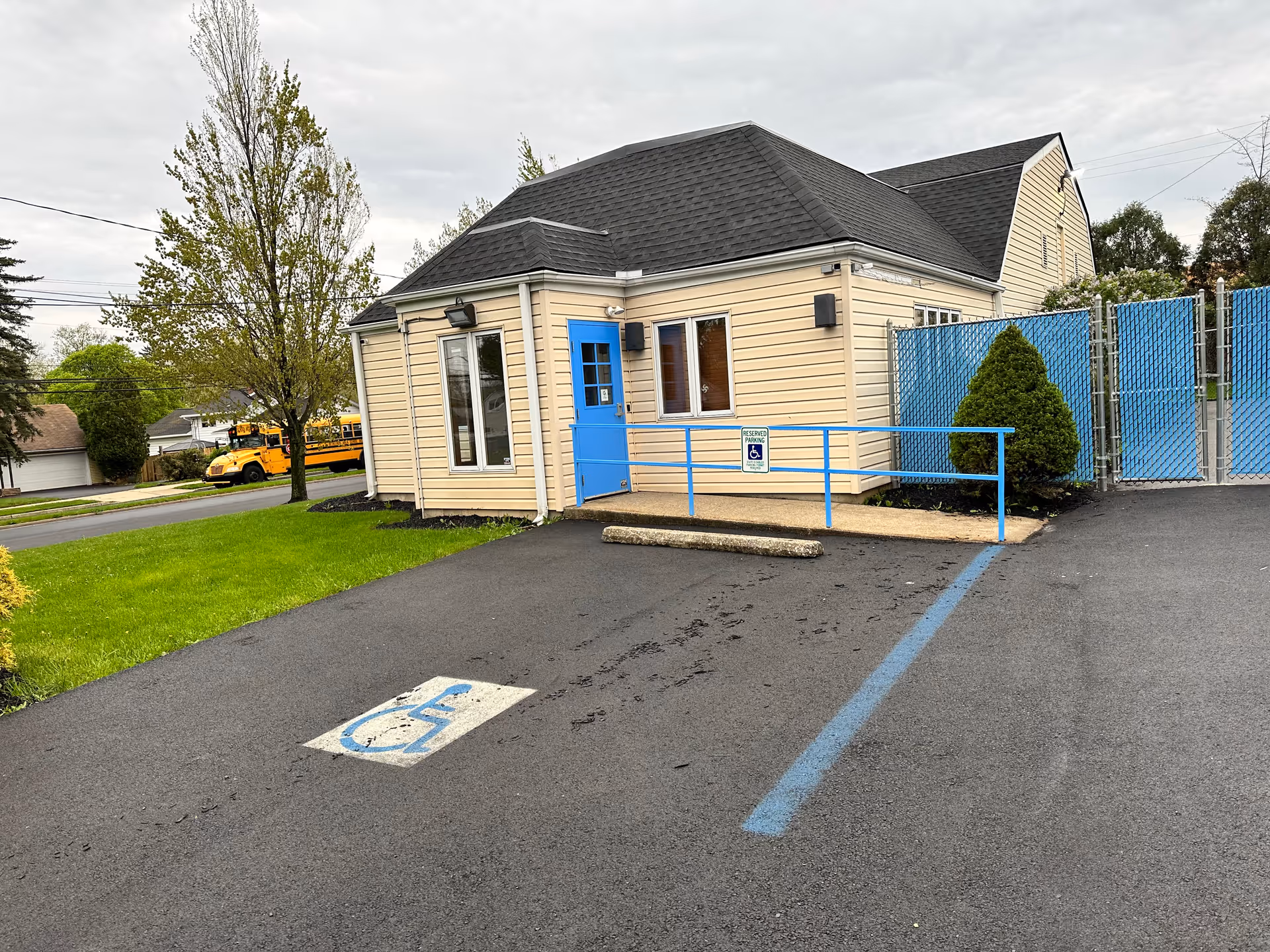 Exterior view of a beige senior care facility with blue door, ramp, and parking lot.