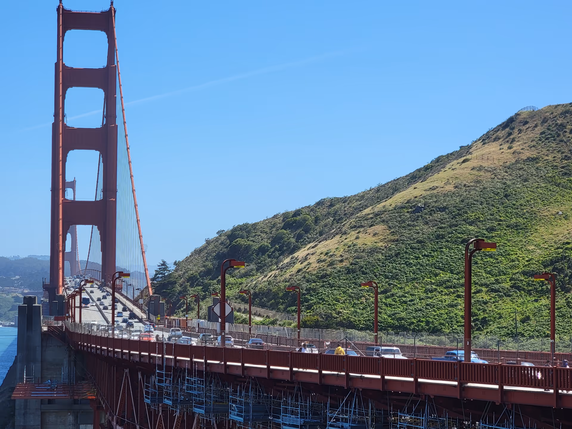 Golden Gate Bridge spans blue sky with traffic over a green hillside.