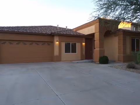 Front exterior of a tan assisted living building with a two-car garage and driveway.