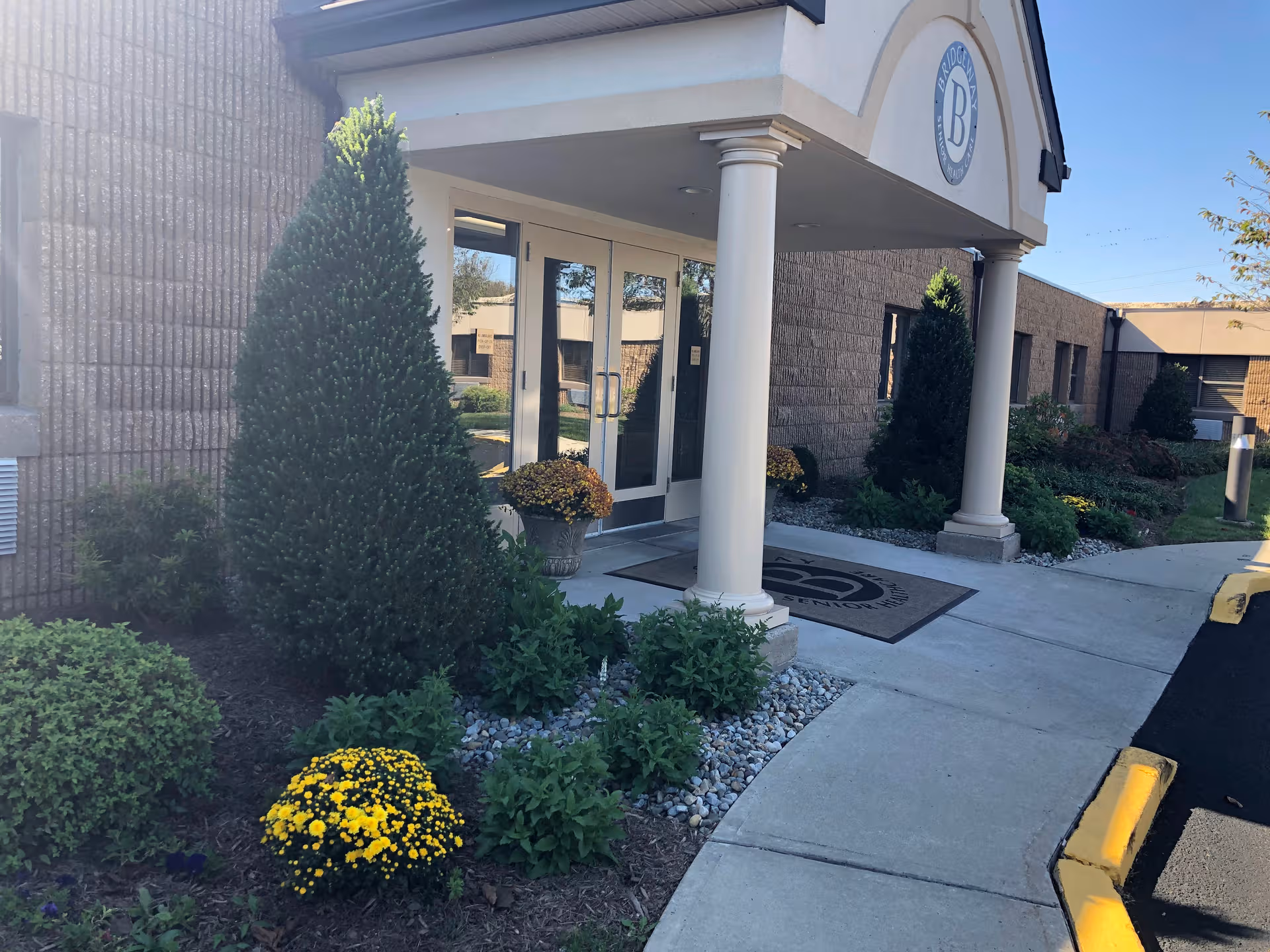 Exterior view of Bridgeway Care and Rehab Bridgewater entrance with columns and landscaped pathway.