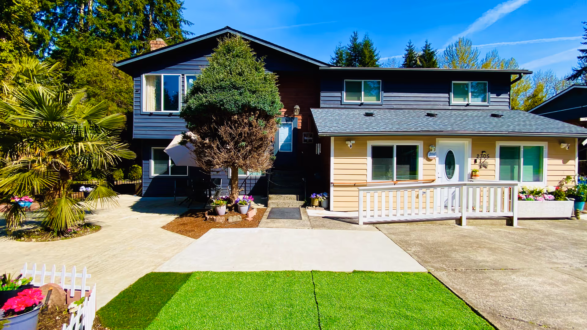 Two-story house-style senior living facility with front porch, ramp, and landscaped yard.