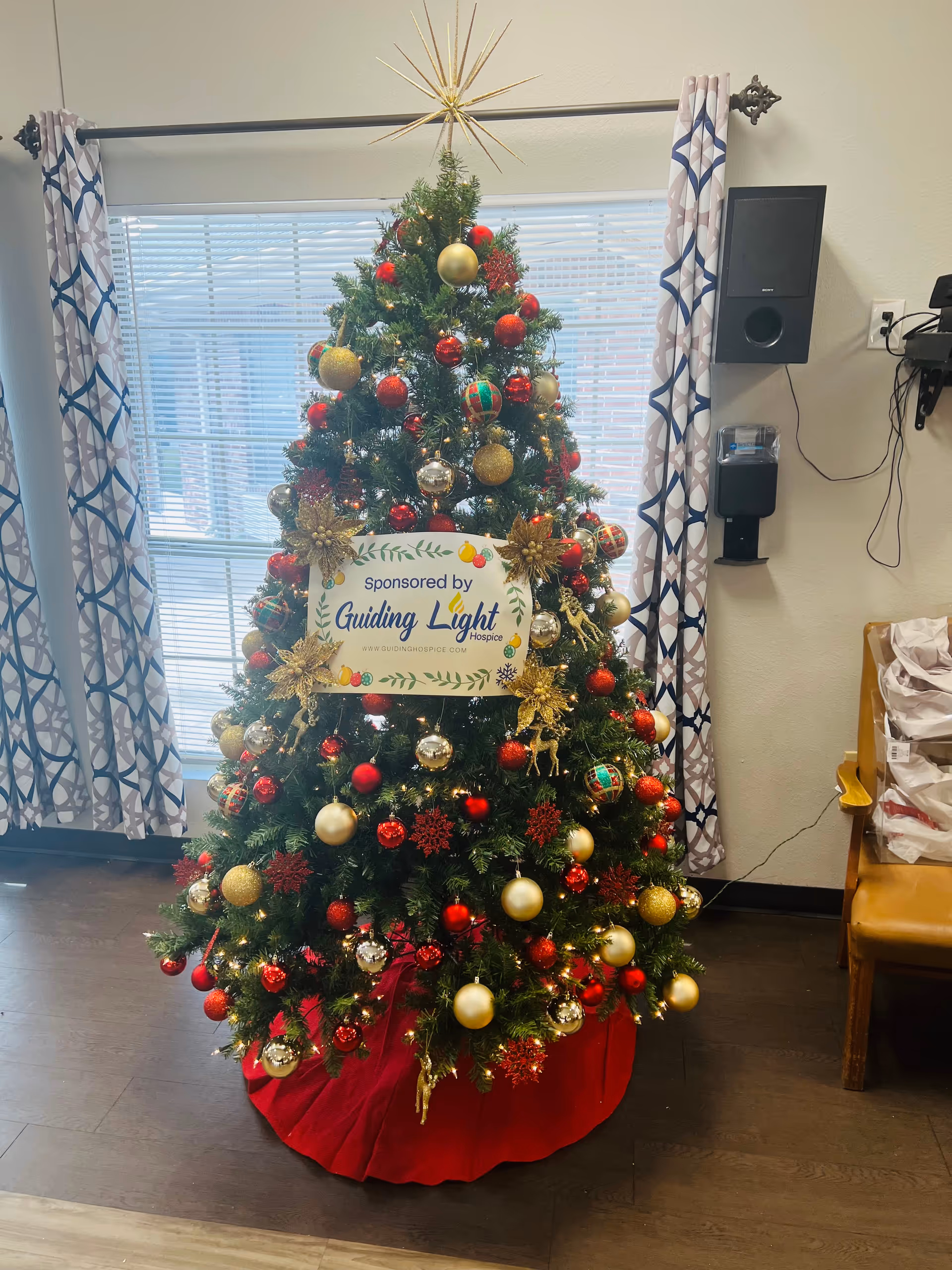 Decorated Christmas tree in an interior facility room with a Guiding Light Hospice sign.