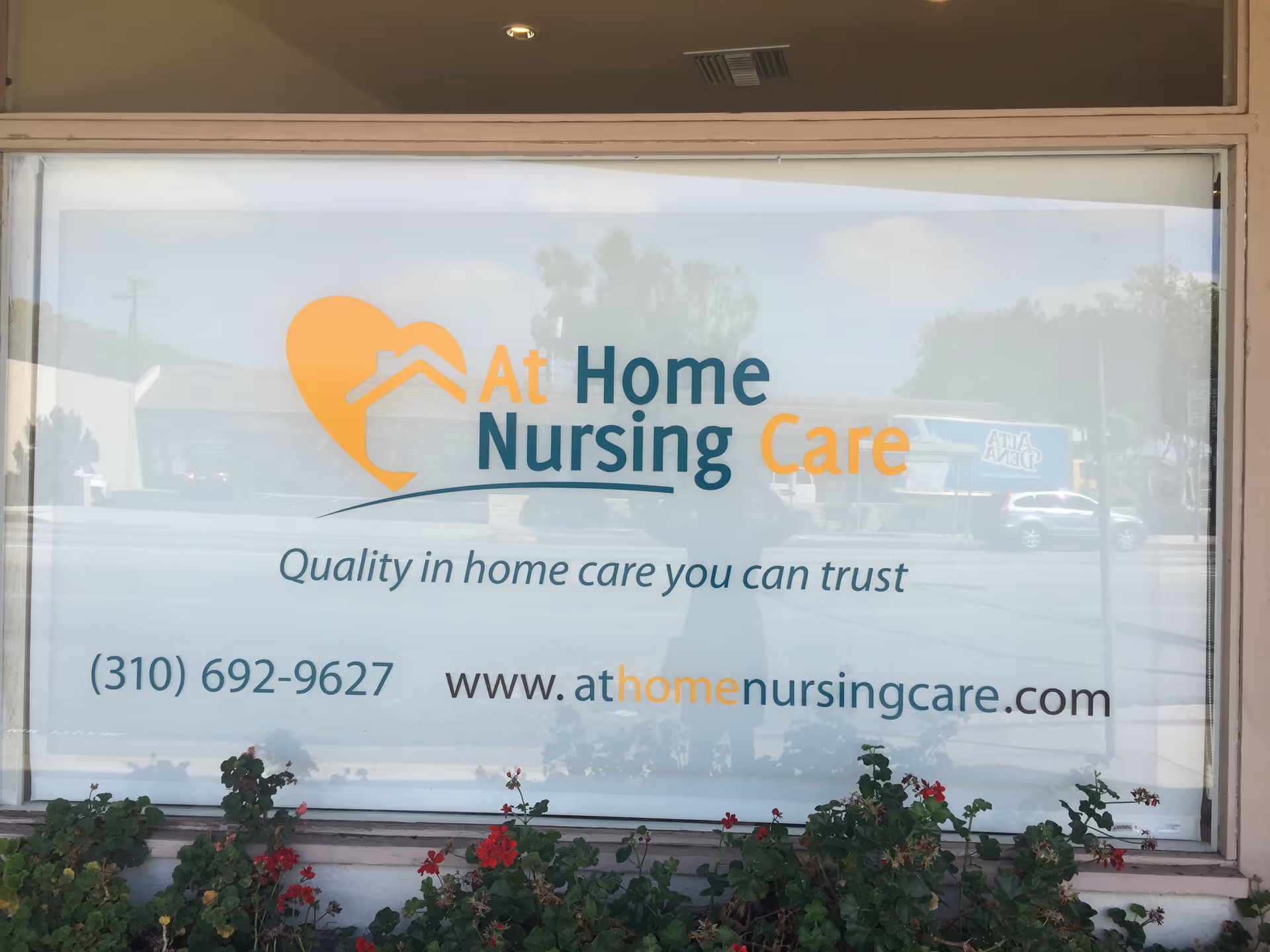 Front window sign for At Home Nursing Care with logo and contact info.