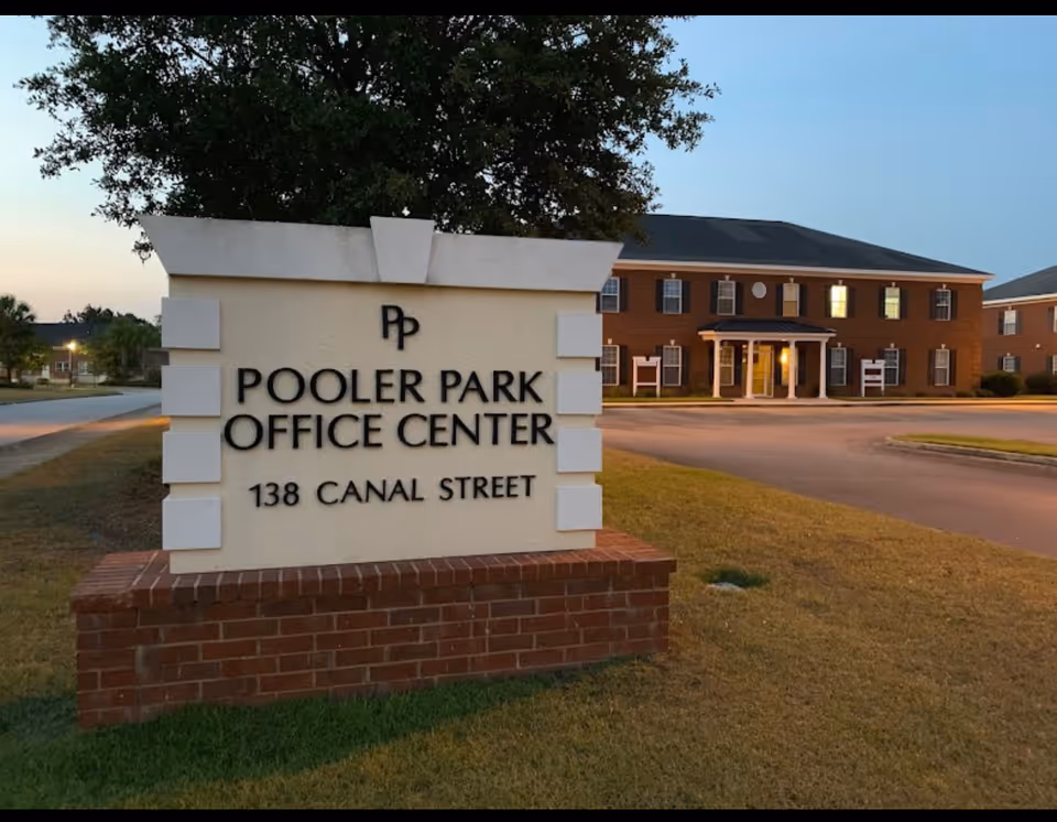 Outdoor scene with a white sign reading Pooler Park Office Center near a brick building.